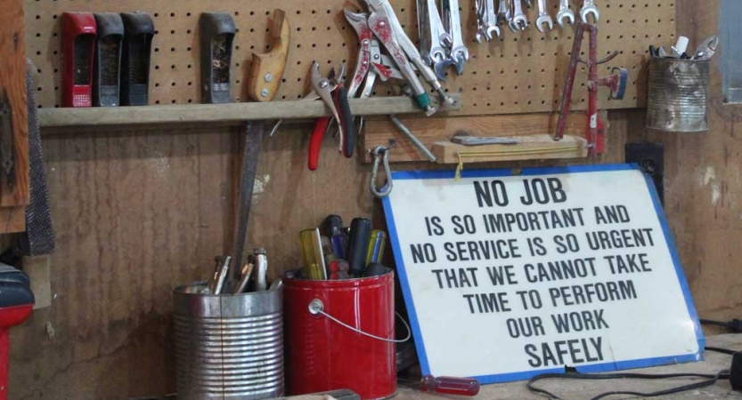 A sign rests on a wall against tools. It reads "No job is so important and no service is so urgent that we cannot take time to perform our work safely."